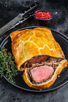 Beef Wellington classic steak dish with tenderloin meat on a plate. Black background. Top view.