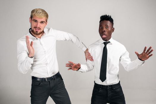 Two stylish men posing and having fun on white background. Friends. Two guys in white shirts and dark pants at studio
