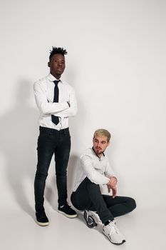 Two stylish men posing and having fun on white background. Friends. Two guys in white shirts and dark pants at studio