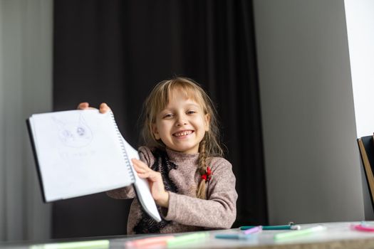 Cute little girl doing her homework, close-up, on home interior background