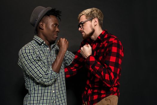 A Friend portraits shot against dark background. Two best friends are posing and having fun in the studio. Dressed in casual clothes, shirts in a cage.