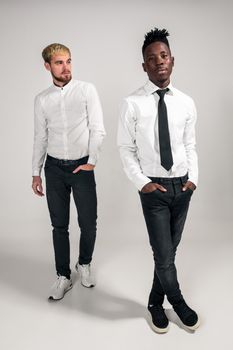 International friendship concept. Studio shot of two stylish young men: handsome bearded young man in white shirt and jeans standing next to his African-American friend on white background