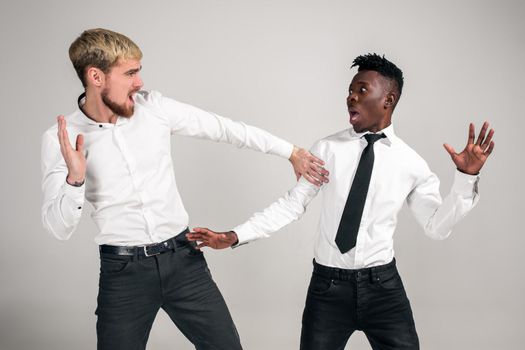Two stylish men posing and having fun on white background. Friends. Two guys in white shirts and dark pants at studio