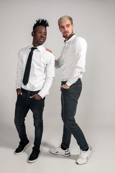 Joyful relaxed african and caucasian boys in white and black office clothes laughing and posing at white studio background with copy space. Full-length photo