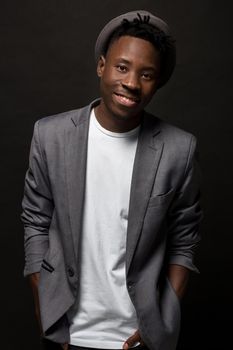 Close-up portrait of handsome black man with charming smile. Studio shot of well-dressed african guy wears hat and jacket, on dark background