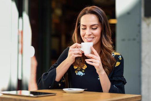 Young woman drinking coffee in an urban cafe bar. Middle-aged female sitting at table at an outside terrace. Girl with california highlights hairstyle.