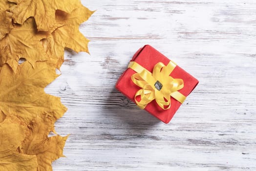 Bright autumn composition with gift box and yellow maple leaves. Holiday present decorated yellow ribbon bow lies on vintage wooden desk. Happy thanksgiving congratulation. Autumn sale advertising.