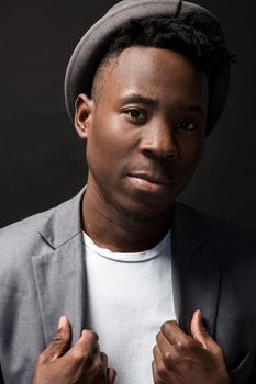 Portrait of a fashionable african american man smiling on black background. A nice guy in a gray jacket and a white T-shirt on a dark studio background. A large portrait