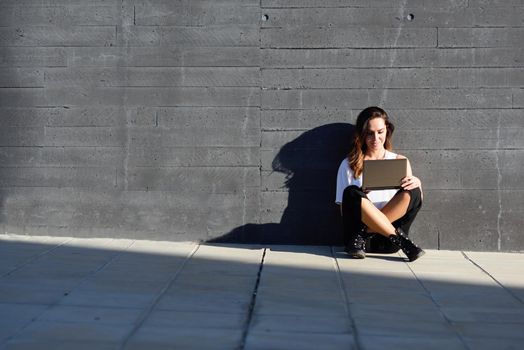 Young businesswoman working with her laptop computer sitting on the floor outdoors.