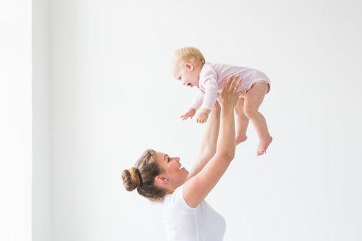 Happy young mother lifting cute baby up high in air, spending and enjoying time together with daughter.