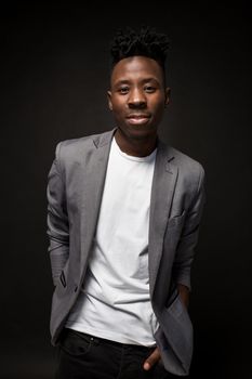 Close-up portrait of handsome black man with charming smile. Studio shot of well-dressed african guy wears white T-shirt and gray jacket, on dark background