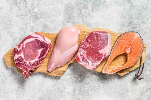 Mix of meat raw steaks salmon, beef, pork and chicken. Gray background. Top view.