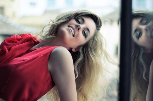 Portrait of a beautiful blonde woman in window wearing a red dress