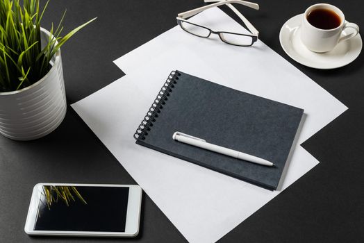 Top view of modern workplace with spiral notepad. Flat lay black surface with smartphone and cup of coffee. Top view coworking workspace and freelance. Digital technology and mobile lifestyle.