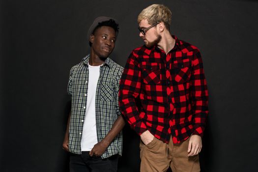 A Friend portraits shot against dark background. Two best friends are posing and having fun in the studio. Dressed in casual clothes, shirts in a cage.