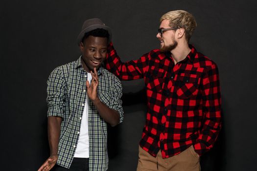 A Friend portraits shot against dark background. Two best friends are posing and having fun in the studio. Dressed in casual clothes, shirts in a cage.