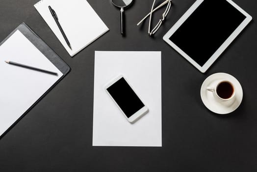 Top view of modern workplace with blank paper sheet. Flat lay black surface with smartphone, notepad and cup of coffee. Top view office workspace and freelance. Digital technology and mobile lifestyle