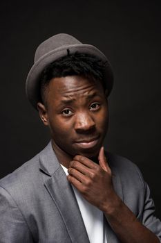 Portrait of a fashionable african american man smiling on black background. A nice guy in a gray jacket and a white T-shirt on a dark studio background. A large portrait