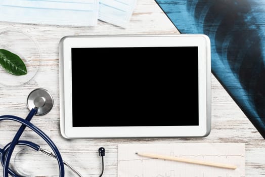 Laboratory result of patient examination lies on doctor table. Top view tablet computer with blank screen, x-ray image, stethoscope and cardiogram on wooden desk. Digital technology in cardiology.