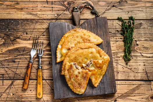 Chilean fried empanadas filled with minced beef meat served on a wooden cutting board. Wooden background. Top view.