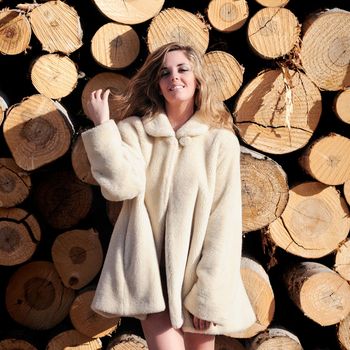 Portrait of a beautiful blonde woman wearing a white coat on poplar trunks