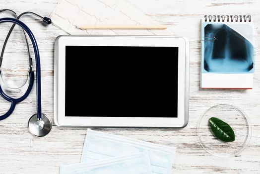 Medical diagnostics in modern hospital. Top view tablet computer with blank screen, x-ray image, stethoscope and cardiogram on wooden desk. Professional healthcare and digital technology in clinic.
