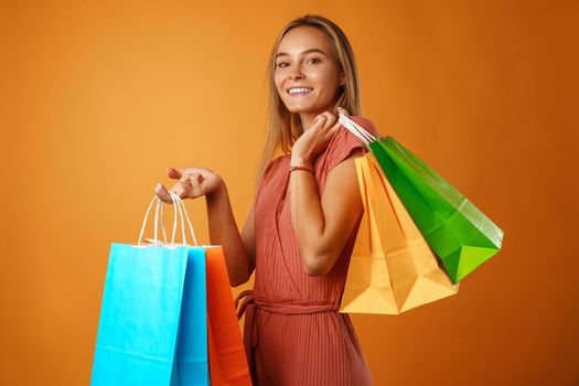 Portrait of happy young smiling woman with shopping bags against orange background