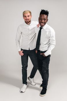 International friendship concept. Studio shot of two stylish young men: handsome bearded young man in white shirt and jeans standing next to his African-American friend on white background
