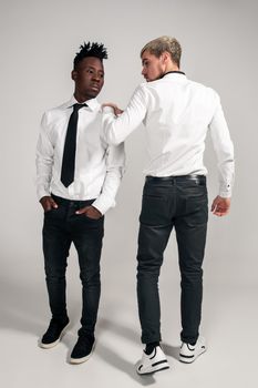 Joyful relaxed african and caucasian boys in white and black office clothes laughing and posing at white studio background with copy space. Full-length photo