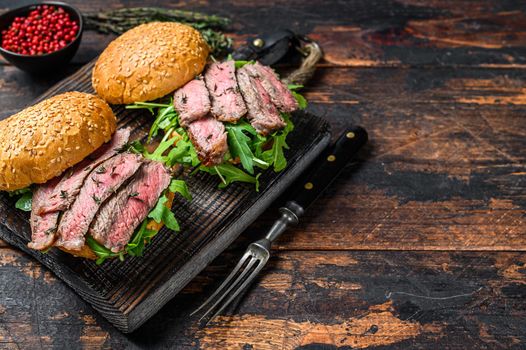 Burger with beef steak slices, arugula and spinach. Dark wooden background. Top view. Copy space.