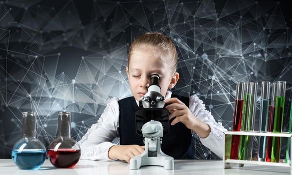 Little girl scientist looking through microscope in classroom at chemistry lesson. School chemical laboratory with glass flasks and test tubes. Schoolgirl making experiment in chemistry class.