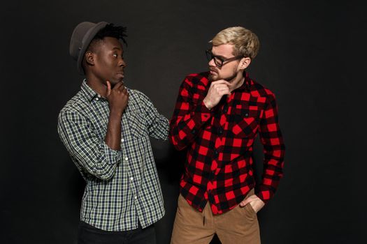 A Friend portraits shot against dark background. Two best friends are posing and having fun in the studio. Dressed in casual clothes, shirts in a cage.