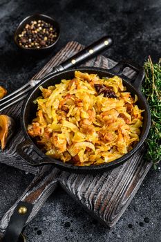 Stewed cabbage Bigos with mushrooms and sausages. Black background. Top view.