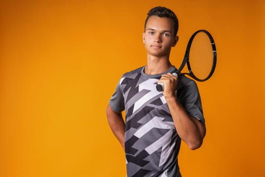 Portrait of a young man tennis player on orange background close up