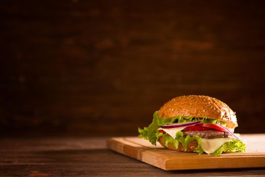 Burger on a wooden board on wooden table over dark background.