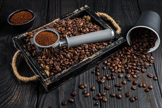 Ground Coffee in Portafilter for Espresso in a wooden tray with coffee beans. Black wooden background. Top view.