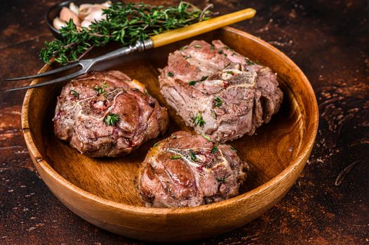 Fried lamb neck meat steaks in a wooden plate with herbs. Dark background. Top view.