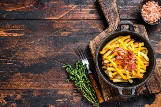 French fries with melted mix of cheddar cheese and bacon served in a pan. Dark wooden background. Top view. Copy space.