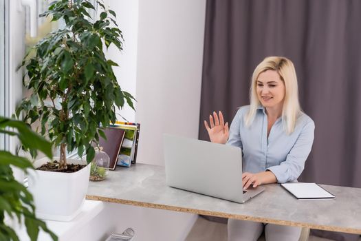 Young woman sitting at her desk in front of a gray laptop while daydreaming of nice memories or future in a modern bright office with large window