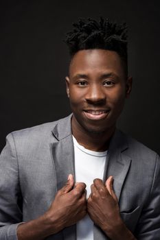 Close-up portrait of handsome black man with charming smile. Studio shot of well-dressed african guy wears white T-shirt and gray jacket, on dark background