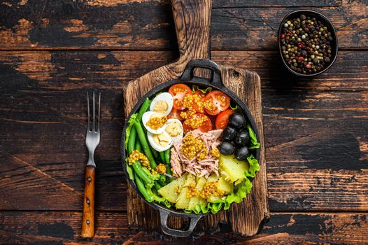 Nicoise salad with tuna, cherry tomatoes, olives, green beans, cucumber, soft boiled eggs and potato. Dark wooden background. top view.