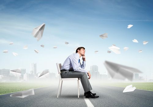 young businessman sits on an office chair, thoughtful and looking up