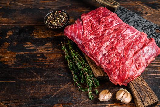 Big piece of raw beef brisket cut meat with herbs and butcher cleaver. Dark wooden background. Top view. Copy space.