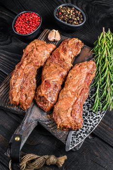 Marinated brisket steaks in bbq sauce on a wooden cutting board with herbs. Black wooden background. Top view.