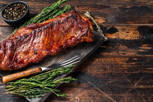 BBQ grilled veal calf brisket meat on short spare rib on wooden cutting board. Dark wooden background. Top view. Copy space.