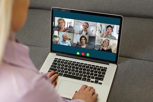 View over businesslady shoulder seated at workplace desk look at computer screen where collage of many diverse people involved at video conference negotiations activity, modern app tech usage concept.