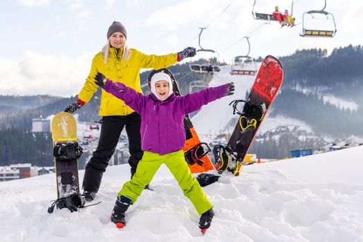 Mother and daughter with snowboards are playing in the snow