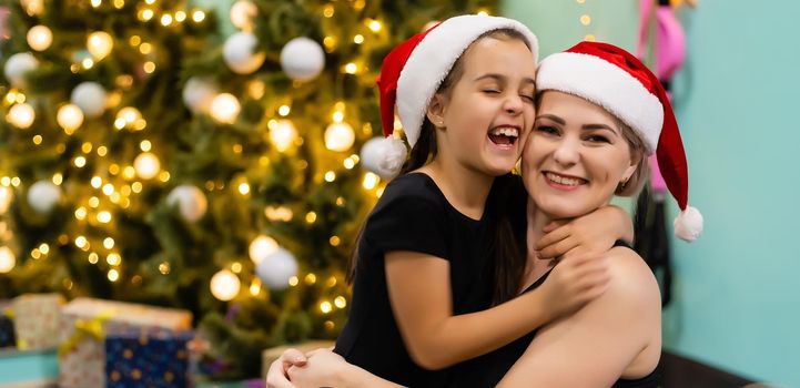 Loving mother and daughter hugging near christmas tree, looking amazing.