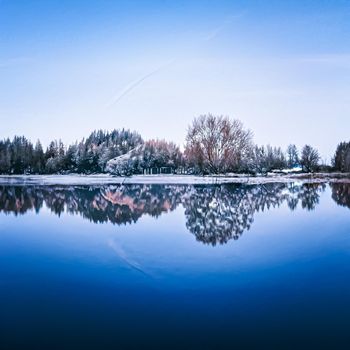 Winter wonderland and Christmas landscape. Frozen lake in snowy mountains and trees covered with snow as holiday background.