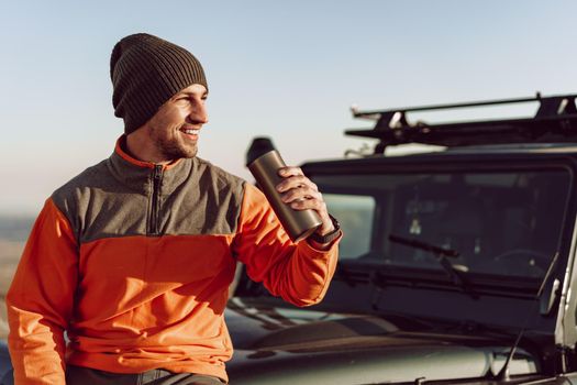 Young man traveler drinking from his thermocup while halt on a hike, close-up portrait